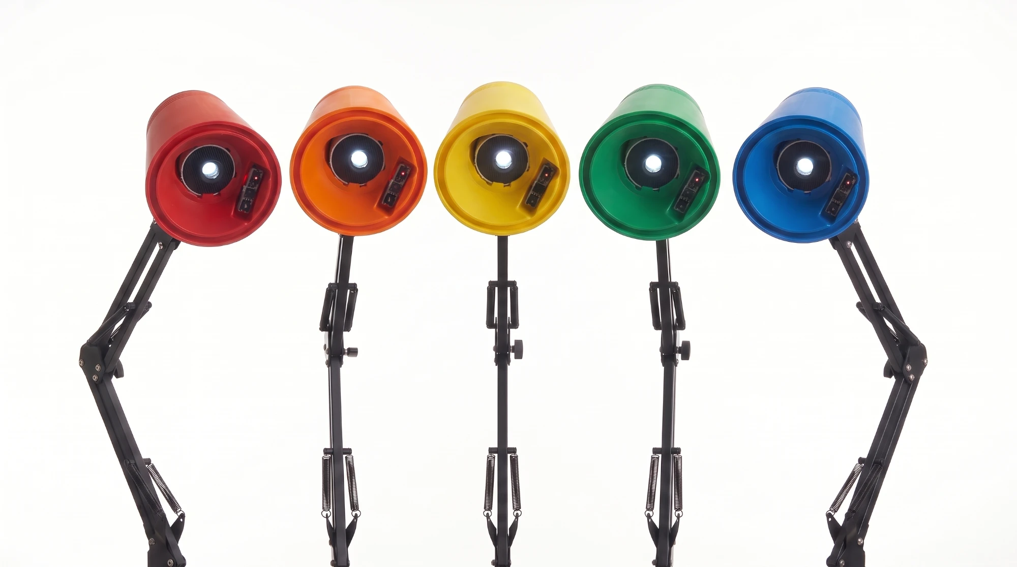 Five Prism lamps in red, orange, yellow, green, and blue, in a row, each facing forward